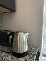 Electric kettle sitting on a granite countertop next to a black toaster.
