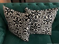 Two black and white decorative square pillows on dark green couch, showing circular medallion pattern