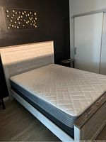 Wooden queen bed frame in white beige color with horizontal panel headboard and footboard, with a quilted mattress on top.