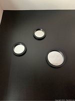 Three round mirrors mounted on a dark wall, showing varying sizes and black frames.