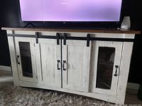 Full front view of the vintage wooden sideboard showing distressed white finish, black hardware, natural wood top, and sliding doors with chicken wire panels.