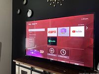 Photo showing TCL Roku TV powered on with the home screen UI visible, displaying various streaming options and apps including ESPN, YouTube, and Spotify.