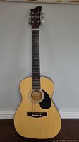 Full front view of the acoustic guitar showing natural wood finish, sound hole, black pickguard, and bridge.