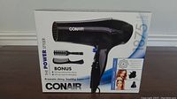 Boxed CONAIR hair dryer with 1875 watts power and bonus brush visible on the packaging, front view.