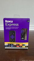 Front view of Roku Express packaging showing the device, remote, and streaming service logos.