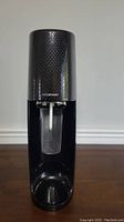 Front view of black Sodastream soda maker with carbonating bottle attached.