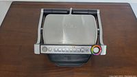 Top-down photo of closed T-fal OptiGrill showing stainless steel lid and black handles.