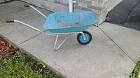 Side view of the light blue metal wheelbarrow showing wheel, handles, and tub with rust spots.