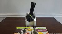 Yonanas ice cream maker on a wooden table with two recipe guide booklets.