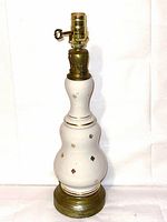 Front view of antique French lamp showing ceramic body with gold fleur de lis decorations and brass base, socket with key switch visible