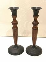 Pair of black bronze metal candlesticks with wooden stems, shown together against a neutral background to illustrate the set.