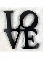 Image showing the black matte LOVE sculpture art piece laying on a white fabric background, with the O tilted diagonally.