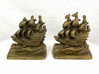 Front view of pair of bronze style brass bookends shaped as sailing ships on waves, showing detailed sails and ship hull.