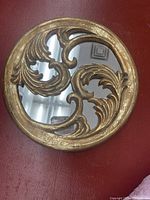 Front view of the round gold mirror with ornate scroll design on the frame.