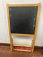 Front side of the easel showing the black chalkboard surface within a natural wood frame, with some paint marks and wear visible on the chalkboard and tray area.