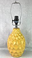 Side view of the yellow ceramic lamp showing the textured diamond pattern and overall shape with metal socket and harp attachment.