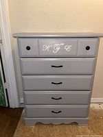 Front angle photo of vintage gray tall dresser showing five drawers with mixed knobs and handle pulls, scalloped base detail.