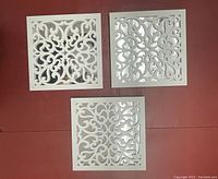 Three white lace cut-out square mirrors arranged together on a red surface showing overall condition and design.