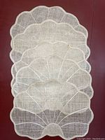 Five stacked woven natural fiber placemats showing fan shape and scalloped edges on maroon surface.