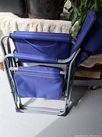 Folded camping chair showing cooler bag attached on side and metal frame folded compact.