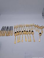 Full layout of the entire golden coloured cutlery set showing knives, forks, spoons and teaspoons.