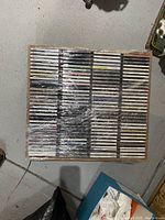 Wooden tray filled with rows of shrink-wrapped CD jewel cases, overhead view.