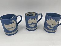 Front view of three Wedgwood Jasperware mugs showing architectural white reliefs on blue base.