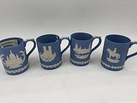 Four Wedgwood blue jasperware mugs with white relief designs, displayed side-by-side showing different landmarks