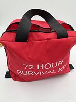 Photo of the closed red soft bag labeling '72 HOUR SURVIVAL KIT',' showing the front with handles and zipper.
