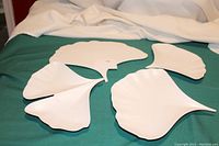 Four white ginkgo leaf-shaped porcelain serving dishes arranged on green cloth with cream draped fabric background, showing various unique leaf shapes.