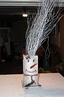 Full view of snowman planter box with white branches and red berries inside