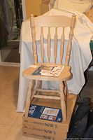 One pre-assembled Country Arrowback chair in natural unfinished wood, with assembly and finishing instructions on the seat, and three boxed kits underneath.