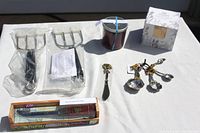 Photo showing two Pampered Chef meat lifters in plastic wrapping, wine art boxed cheese knife, scented candle in box, and measuring spoons.