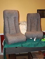 Pair of gray fabric-covered floor rocker gaming/lounge chairs with a textured wave pattern displayed on a green surface, showing seating area, backrest, and overall shape.