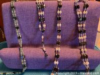 Four magnetic jewelry pieces including two black, brown, and pearl sets, one green and black set, and one black and pearl set displayed on purple fabric.