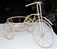 Front side view of the metal tricycle-shaped plant stand on a white surface, showing the full tricycle frame with planter holder on the back.