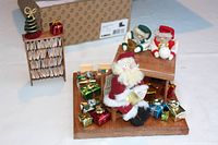 Angle showing Santa figure holding a book, surrounded by many miniature wrapped gifts and elves at a workbench.