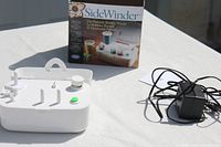 Photo showing the bobbin winder unit, power adapter, and instruction manual laid out on a surface.