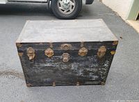 Full view of the vintage black steamer trunk showing weathered exterior and metal hardware.
