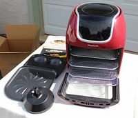 Overview of PowerXL Vortex Air Fryer Pro with three metal mesh racks inside tray, muffin pan, rotisserie stand, and instruction manuals visible.