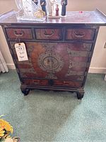 Front view of the antique cabinet showing three drawers on top, two large doors below with metal hardware and decorative medallion in the center.