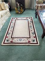 Full view of the rectangular floral border area rug laid on green carpet in a living room setting.