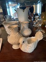 Photo showing three small vases with gold rims, a white bird figurine, a pierced design container, and a larger vase in the background.