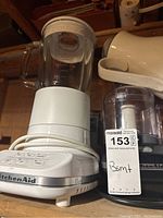 Photo showing KitchenAid blender with clear glass jar, white base with buttons, and cord wrapped around base.