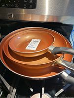 Stacked set of 3 copper frying pans showing exterior copper coloration and black handles.