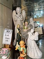 Photo showing an assortment of angel and child figurines, embracing couple figurine, and floral ceramic piece.