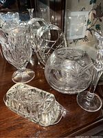 Photo showing several clear glass and crystal items including a large footed vase, two round bowls, a butter dish with lid, and a tall candlestick holder all with intricate cut patterns.