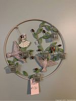 Circular metal wall art piece featuring birds, a ballerina figure, and glass candle holders, with painted leaves and branches.