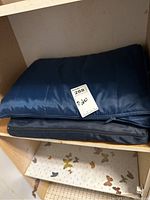 Folded navy blue picnic blankets inside a shelf, showing one with a zipper and smooth quilted fabric.