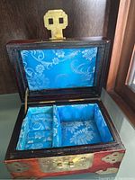 Photo of an open wooden jewelry box, showing blue floral fabric lining with compartments for rings and storage.